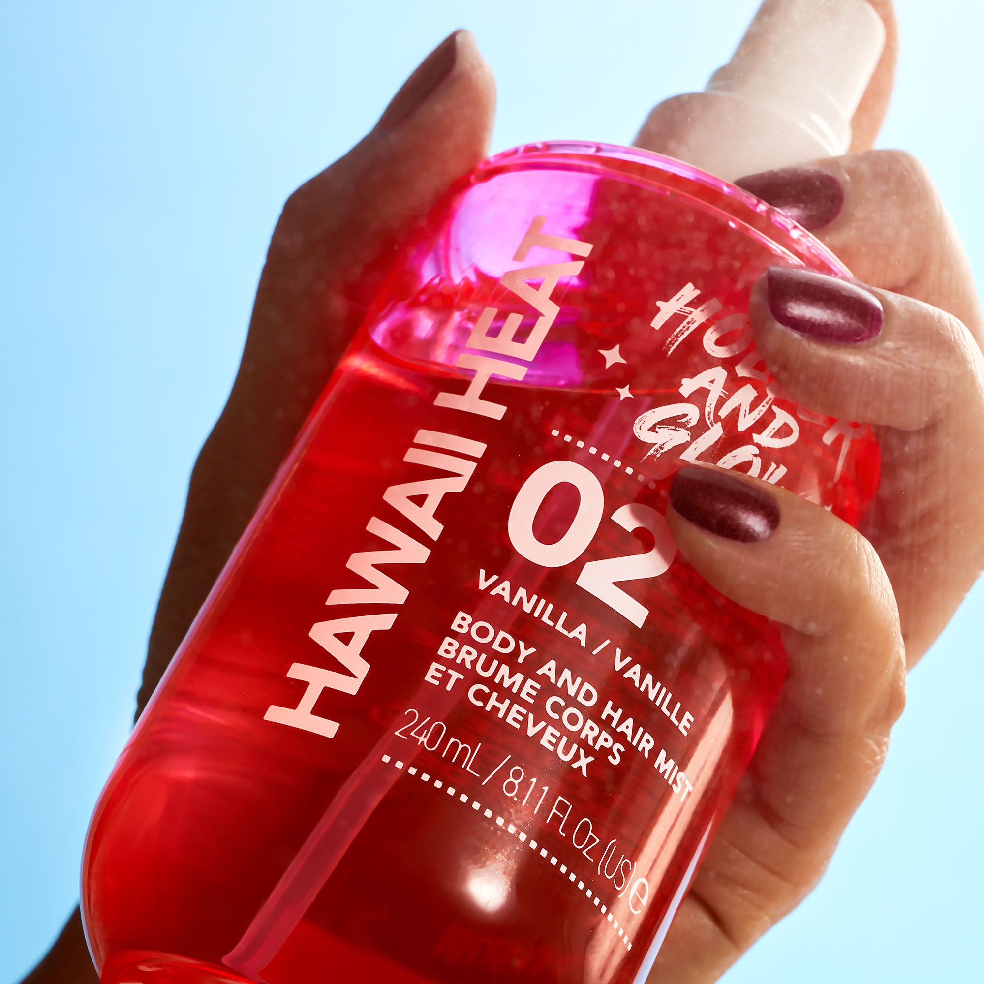 Hand holding a red bottle of 'Hawaii Heat' product against a clear blue sky.