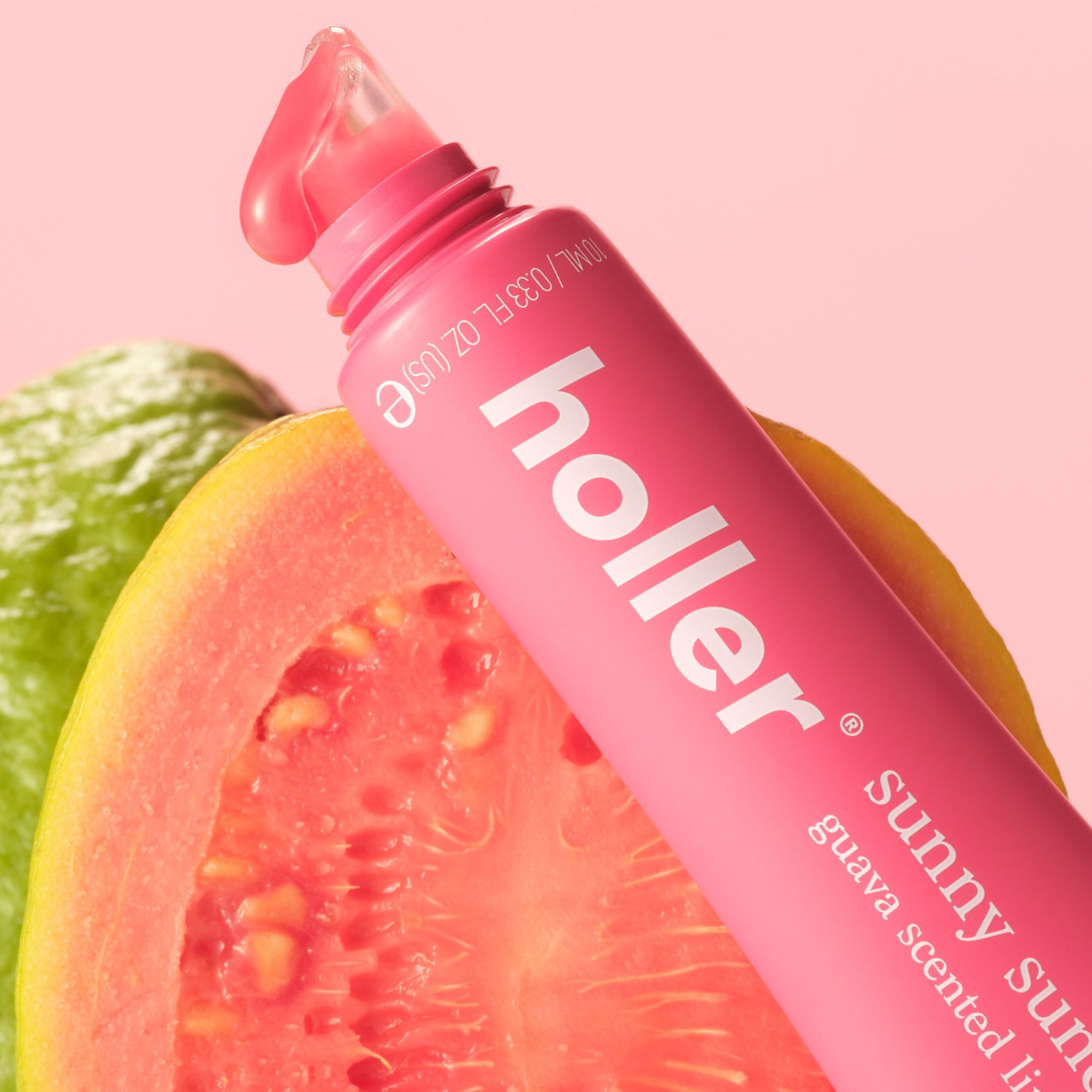 Pink 'holler' lip gloss with guava fruit on a pink background