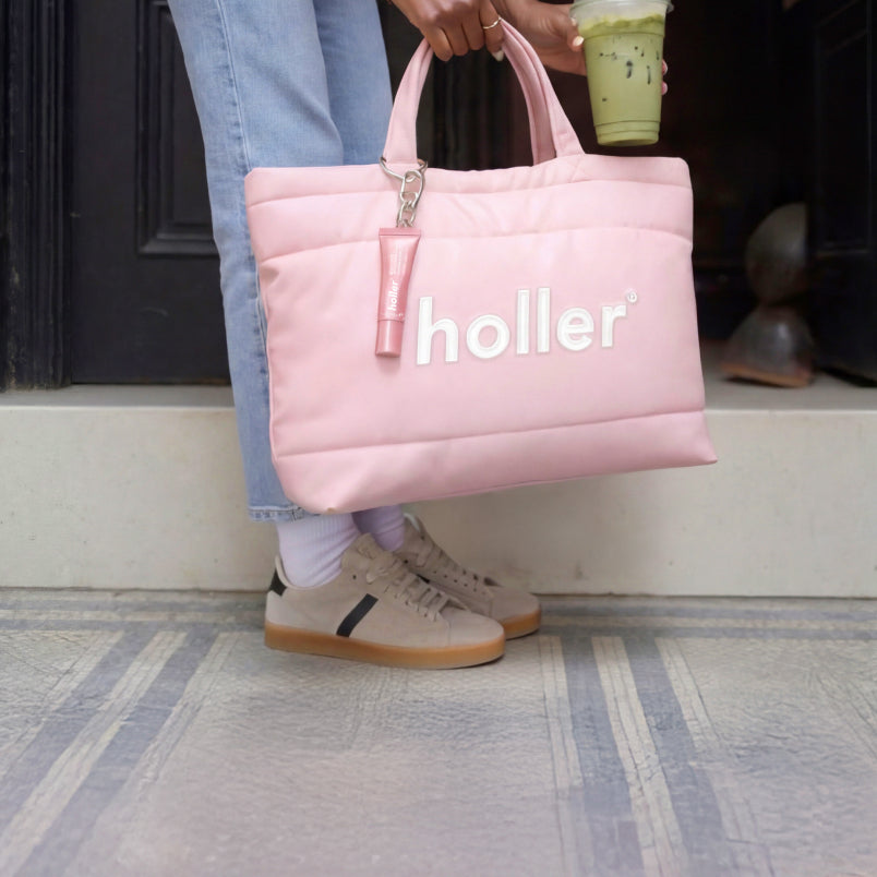 Person holding a pink bag with 'holler' branding, standing on a step.